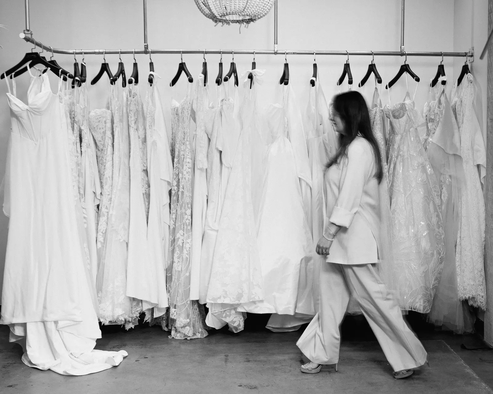 A boutique owner walking the sales floor between rails of wedding gowns at Cande Bridal Boutique