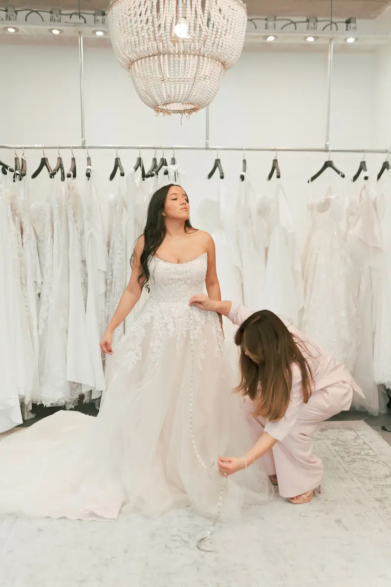 A bride being fitted into a gown by a consultant during a booked appointment at a bridal boutique