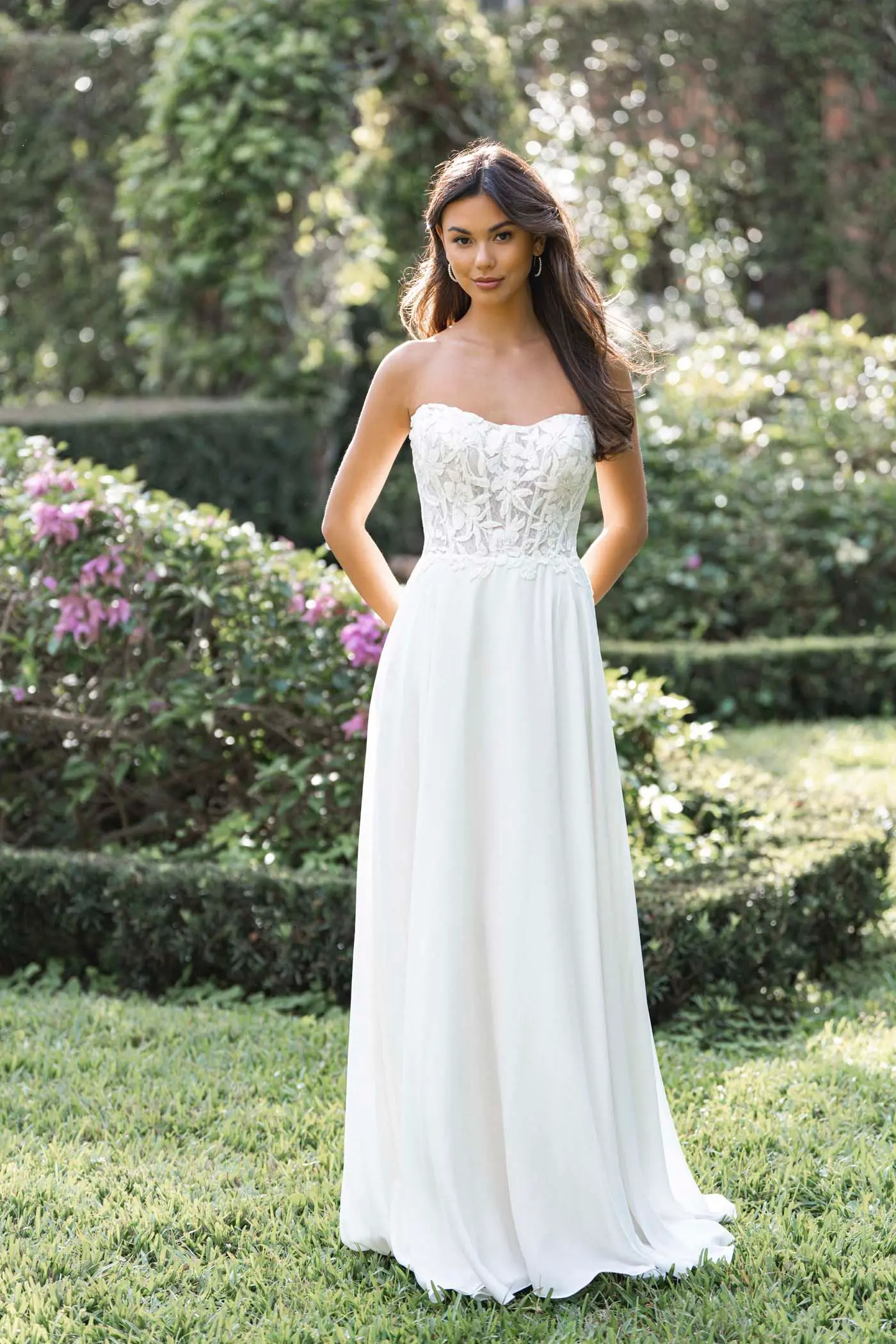 Bride in a strapless Romance gown with a floral lace bodice and a soft A-line skirt, standing in a garden